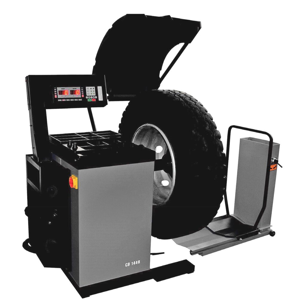 Professionelle Lkw-Radauswuchtmaschine mit montiertem Nutzfahrzeugreifen, digitalem Bedienpanel, Schutzhaube, integriertem Ablagetisch und seitlicher Hebeplattform für schwere Räder.