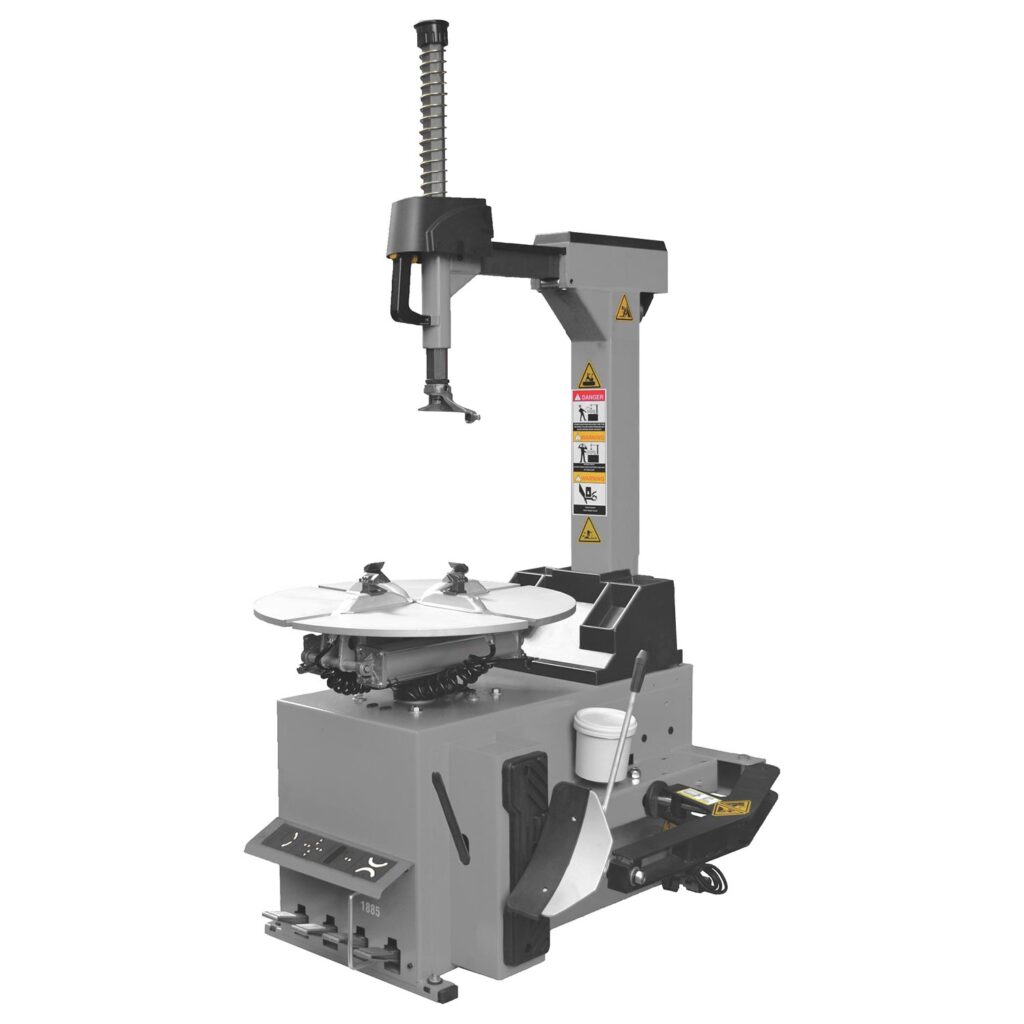 Automatische Reifenmontiermaschine mit vertikalem Montagearm, rotierendem Drehteller, integrierter Abdrückeinheit und Bedienelementen, graue Industriekonstruktion vor weißem Hintergrund.